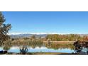 Scenic lake view with mature trees in foreground and snow capped mountains in the distance at 10667 E Goose Haven Dr, Lafayette, CO 80026