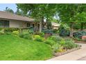 Beautifully landscaped front yard with lush green grass, colorful flowers, bushes, and mature trees at 3401 E Kentucky Ave, Denver, CO 80209