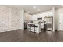 Modern kitchen featuring stainless steel appliances, a granite island with bar stools, and an exposed brick wall at 1353 Reynolds St # 16B, Fort Lupton, CO 80621