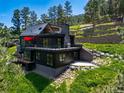 Gorgeous modern home displays a stunning outdoor deck, patio, and unique architectural design amid green landscaping at 365 Bow Mountain Rd, Boulder, CO 80302