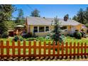 Charming yellow home with a gray roof, manicured lawn, and a decorative wooden fence at 4805 S Blue Spruce Rd, Evergreen, CO 80439