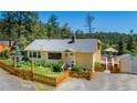 Charming yellow home featuring a cozy front porch, well-maintained lawn and a cute, decorative wooden fence at 4805 S Blue Spruce Rd, Evergreen, CO 80439