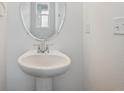 White pedestal sink with a round mirror and chrome faucet in a minimalist powder room at 170 Lark Sparrow Way, Bennett, CO 80102