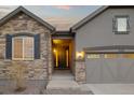 Inviting entryway with stone accents, a gray three-car garage, and a well-lit front door at 6514 Agave Ave, Castle Rock, CO 80108