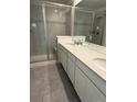 Modern bathroom featuring double sinks, white cabinets, gray tile flooring, and a glass-enclosed shower at 9041 Redfield Ln, Parker, CO 80134