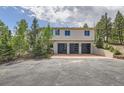 Three-car garage with modern doors and a spacious driveway with steps leading to the home's entrance at 30671 Bearcat Trl, Conifer, CO 80433