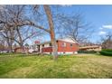 Side view of a red brick single-story home featuring a well-maintained lawn and a tree in the foreground at 13373 W 24Th Pl, Golden, CO 80401