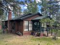 Rustic cabin exterior featuring a covered porch, brick chimney, and lush green surroundings at 4393 Pima Rd, Indian Hills, CO 80454
