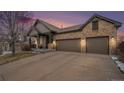 Exterior view of a brick home with a two-car garage at sunset showing the covered front porch at 7262 Serena Dr, Castle Pines, CO 80108