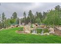 Landscaped backyard featuring a pond and tennis court, surrounded by lush greenery and trees at 34650 Sleeping Fox Trl, Evergreen, CO 80439