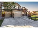 Inviting home featuring a three-car garage, stone accents, and manicured lawn at sunset at 15310 E 108Th Way, Commerce City, CO 80022
