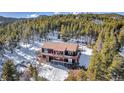 Drone view of a picturesque cabin nestled in a snowy forest with an expansive wooden deck at 255 Divide View Dr, Golden, CO 80403