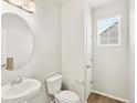 Compact bathroom with round mirror, pedestal sink, toilet, white walls, and window at 17120 E 90Th Pl, Commerce City, CO 80022