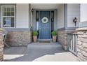Close-up of the front porch with stone accents, a blue door with a wreath, and potted plants at 703 Tiger Lily Way, Highlands Ranch, CO 80126