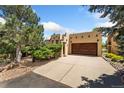This tan home features a large driveway, wood garage door, and Southwestern architectural details at 6457 Willow Broom Trl, Littleton, CO 80125