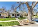 A charming white brick home is framed by a large tree and a well-manicured lawn on a sunny day at 4551 Julian St, Denver, CO 80211