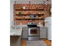 Cozy kitchen features stainless steel appliances, gray cabinetry, brick wall accent, and stylish open shelving at 2424 N Clay St, Denver, CO 80211