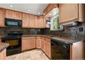 Kitchen featuring wood cabinets, mosaic backsplash, black appliances, and a window over the sink at 8679 Apache Plume Dr, Parker, CO 80134