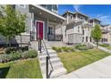 Close-up of a modern townhome featuring gray siding, stone accents, a red front door, and landscaping at 12314 Hayloft Ln, Thornton, CO 80241