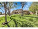 Beautiful brick home with a lush green lawn, mature trees, and a serene setting on a sunny day at 6116 W Frost Dr, Littleton, CO 80128