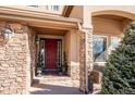 Inviting front entrance with a red door, stone pillars, and manicured greenery enhancing the curb appeal at 16403 River Haven Way, Morrison, CO 80465
