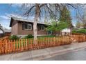 Traditional brick house with a picket fence, green lawn, mature trees, and a two-car garage with an extended driveway at 3150 S Pitkin St, Aurora, CO 80013