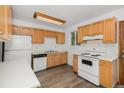 Functional kitchen with wood cabinets, white appliances, and wood-look vinyl flooring at 4678 S Lewiston Way, Aurora, CO 80015