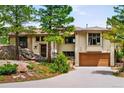 Well-maintained home with stucco exterior, brown garage doors, mature trees, and natural rock formations at 8932 Eastridge Rd, Golden, CO 80403