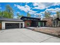 Modern home features a stone chimney, black trim, wood accents, a black garage door, and a spacious driveway at 6260 Lamar St, Arvada, CO 80003
