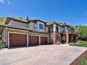 Large driveway leading to a three car garage with stone accents and lush landscaping at 6405 Warriors Run, Littleton, CO 80125