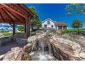 Beautiful backyard featuring a waterfall, stone features, and a home with a three-car garage and well-manicured lawn at 6234 Nautique Cir, Larkspur, CO 80118