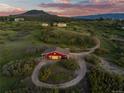 Aerial view of a charming red barn with a circular driveway nestled within a lush, green landscape at 3485 Park Ridge Rd, Sedalia, CO 80135
