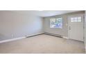 Empty living room showcasing neutral carpet, baseboard heat, large window, and exterior door at 4812 W 8Th Ave, Denver, CO 80204