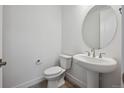 Modern powder room featuring a pedestal sink, round mirror, and a sleek toilet at 1376 Lumber Ridge N Cir, Erie, CO 80516