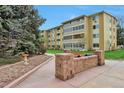 Multi-story tan apartment building featuring patios and well-maintained green spaces and mature trees at 9340 E Center Ave # 8A, Denver, CO 80247
