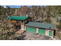 Stunning exterior view of a log home with a green metal roof and a two-car garage, nestled among mature trees at 27231 Log Trl, Conifer, CO 80433