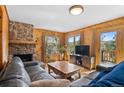 Cozy living room with a stone fireplace, wood-paneled walls, and large windows offering serene outdoor views at 27231 Log Trl, Conifer, CO 80433