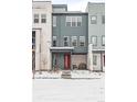 Stylish townhome featuring a modern facade, red door, covered entrance, and snowy yard at 10088 E 62Nd Ave, Denver, CO 80238