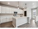 Bright kitchen featuring white cabinets, stainless appliances, a spacious island, and wood grain flooring at 2267 Peregrine Dr, Brighton, CO 80601