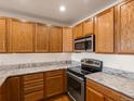 Galley kitchen boasts oak cabinetry, granite counters, and modern black appliances at 6000 W Floyd Ave # 105, Denver, CO 80227