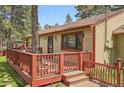 Exterior view of a tan home featuring a wooden deck and mature trees, nestled among lush greenery at 30400 Hilltop Dr, Evergreen, CO 80439