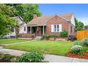 Brick home featuring a cozy front porch, manicured lawn, and vibrant garden beds, enhancing its curb appeal at 1429 Hudson St, Denver, CO 80220