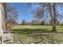 Expansive backyard featuring a lush lawn, mature trees, and a cozy white bench, perfect for outdoor relaxation at 6396 Twin Lakes Rd, Boulder, CO 80301