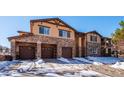 Tan and stone three-story townhouse with three-car garage and snowy landscape at 9876 W Freiburg Dr # G, Littleton, CO 80127