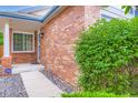 A close up of the brick exterior leading to the front door and window, lush green shrubs, and dark rocks at 2247 S Lima Ct, Aurora, CO 80014