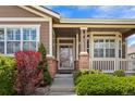 Close-up of the front porch featuring brick columns, a white railing, and colorful foliage at 21780 E Heritage Pkwy, Aurora, CO 80016
