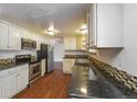 Well-lit kitchen featuring stainless steel appliances, black counters, and warm wood floors at 17209 E Evans Dr, Aurora, CO 80013