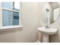 Well-lit half-bath with modern pedestal sink and stylish, round mirror at 19038 E 94Th Pl, Commerce City, CO 80022