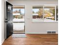 Bright entryway with hardwood floors, a black front door, and a large window view of the snow covered front yard at 7555 E 22Nd Ave, Denver, CO 80207