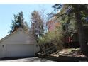 View of a white garage with an automatic door, complemented by landscaped bushes and tall pine trees at 28650 Cavan Ln, Evergreen, CO 80439